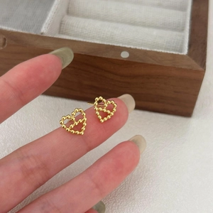 Minimalist 925 silver heart stud earrings with gold granulation texture on fingertip