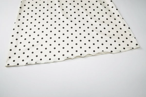 Close-up of white fabric with black polka dots and wavy hemline detail for women's dress
