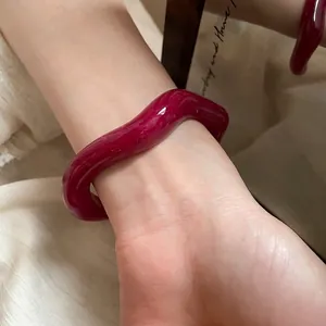 Irregular burgundy wavy bangle with glossy finish shown on wrist in artistic setting