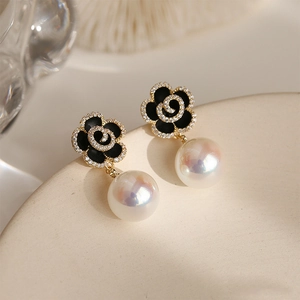 Detail shot of black enamel camellia earrings with pavé diamonds and a lustrous pearl drop