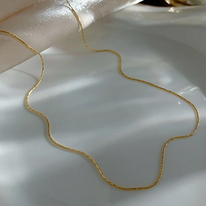 Detailed view of a sleek gold snake chain necklace on white silk with elegant shadows