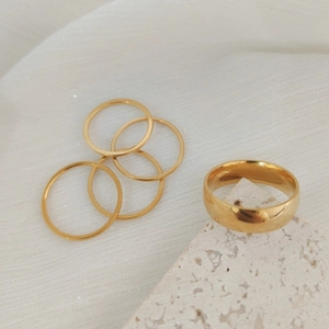 Minimalist stackable gold ring set with one wide band and four thin rings on a stone base