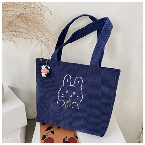 Detail of dark blue corduroy handbag featuring cute rabbit embroidery and cow plush charm