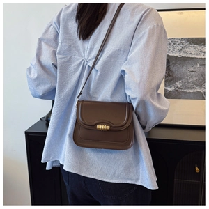 Petit sac à bandoulière marron rétro en cuir avec fermoir doré porté par un modèle