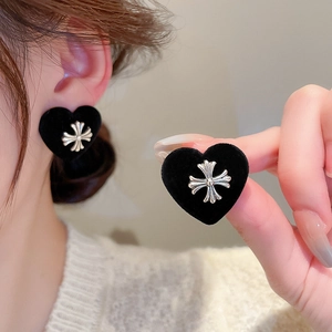 Detail of heart-shaped black flocked earrings with a gothic silver cross emblem
