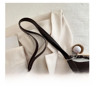 Detail of adjustable shoulder strap and baseball pendant on dark brown leather tote bag