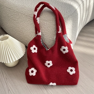 Detail of a red plush tote bag featuring white embroidered flowers and check lining