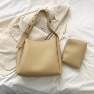 Detail view of beige leather tote bag with inner pouch on minimalist white bedding