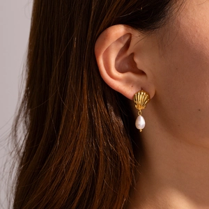 Close-up of a gold shell earring with a teardrop pearl pendant worn by a female model