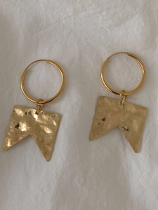 Detailed close-up of golden geometric earrings with hammered texture on white linen