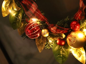 Close-up of Christmas wreath with plaid bow, ornaments, and glowing warm LED fairy lights