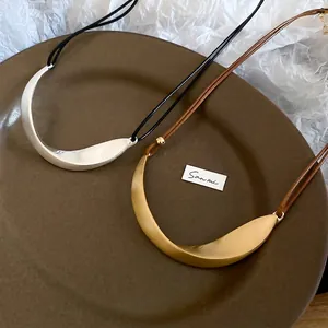 Minimalist matte metal crescent necklaces in gold and silver on a textured background