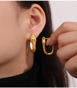 Close-up of golden snake U-shaped earring with green stone eye and detailed scale texture