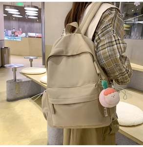 Detail of beige nylon backpack featuring front zipper pocket and cute peach plush pendant