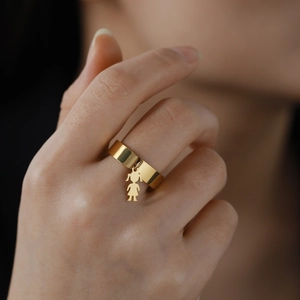 Gold wide band ring with a small girl pendant worn by a model on a soft background