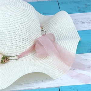 Detailed macro view of white woven straw hat with pink floral ribbon and chiffon decor