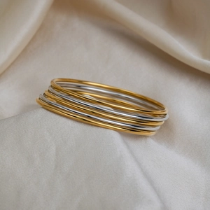 Detail of 18K gold and silver plated stainless steel bangles set on silk background