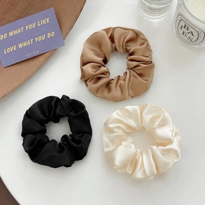 Close-up of three satin scrunchies in champagne, black and white on a desktop