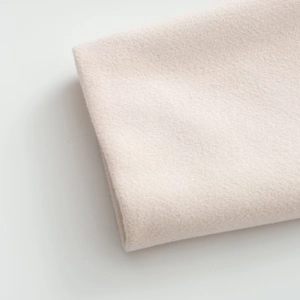 Détail de la texture douce du tissu en laine rose clair sur un manteau d'hiver croisé