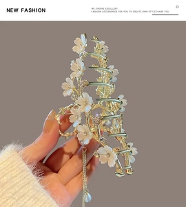 Close-up of golden shark clip with white flowers, chain tassels and faux pearl details
