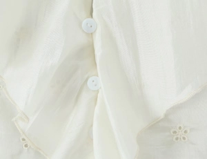 Detail shot of white layered ruffle top featuring delicate floral eyelet embroidery and buttons