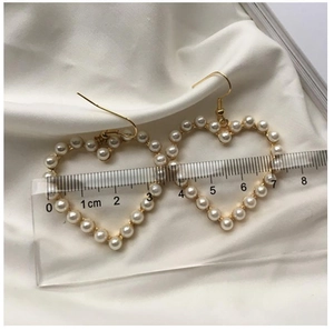Macro shot of 4.5cm heart-shaped pearl drop earrings on white silk fabric background