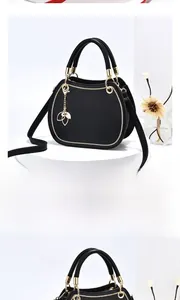 Detail of black handbag with golden leaf charm and adjustable shoulder strap on white stand