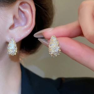 Close-up of gold pear-shaped stud earrings with sparkling white zircons on hand