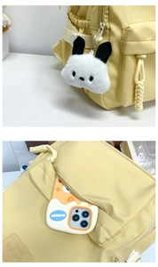 Detail of yellow nylon backpack featuring side pockets, buckle, and plush cartoon pendant
