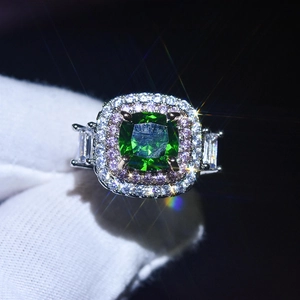Macro shot of silver ring with green emerald cut center stone and pink pavé halo detail