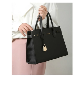 Detail of black pebbled leather tote bag with gold studs on a model in casual outfit