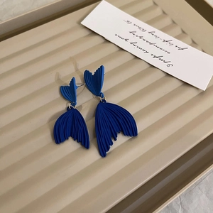 Detail of matte Klein blue fishtail earrings with golden metal rings and fine texture