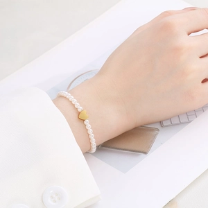 Detailed close-up of an elegant pearl bracelet featuring a gold heart charm on a wrist