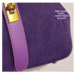 Macro shot of purple suede handbag texture with white stitching and gold metal twist lock