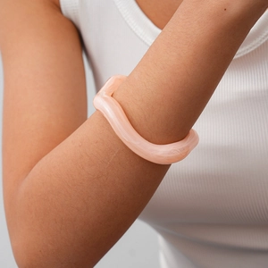 Detail view of pink acrylic wavy bangle on model arm with minimalist aesthetic