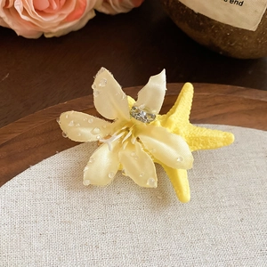 Detailed close-up of yellow fabric flower hair clip with raffia starfish and dewdrops