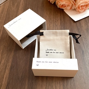 Detailed view of white jewelry gift box and canvas drawstring bag on wooden table