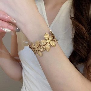 Dettaglio del bracciale a polsino con fiori dorati e petali incisi indossato al polso
