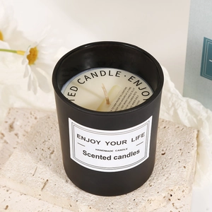 Romantic scented soy candle in black frosted glass jar with wood lid on stone base