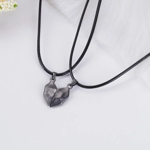 Detail of matte black magnetic heart pendants with black leather cords on floral background