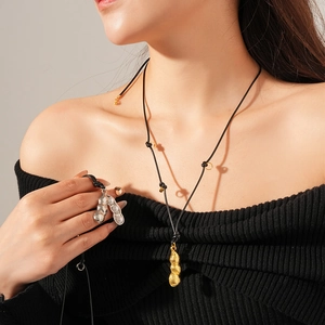 Détail de pendentifs cosses de pois dorés et argentés avec perles sur cordons noirs