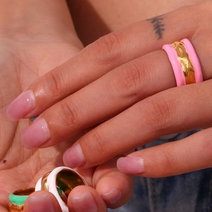 Macro detail of hand wearing stacked gold rings with pink white and green enamel wave texture