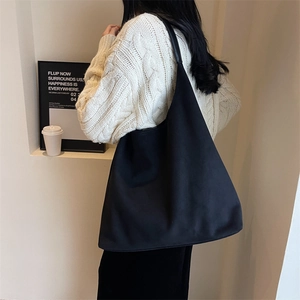 Minimalist black tote bag with wide shoulder strap shown on model in a stylish setting