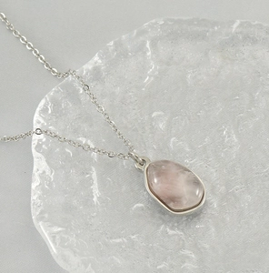 Macro detail of teardrop pink stone pendant with silver edging on a delicate chain