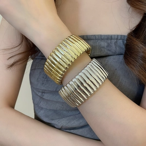 Macro detail of textured ribbed wide metal bangles in gold and silver finish on model
