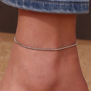 Detailed close-up of a silver stainless steel S-link anklet worn on a model's ankle