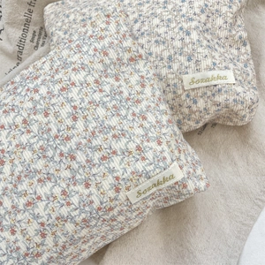 Close-up of quilted floral corduroy pouches with brand labels on natural linen background