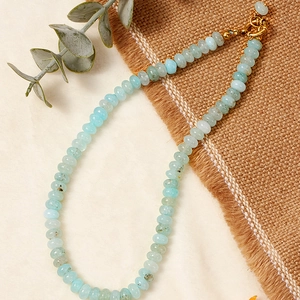 Aquamarine crystal beaded necklace with golden round clasp on rustic linen background