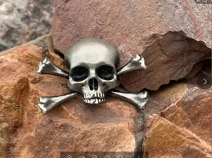 Detail shot of vintage silver skull and crossbones brooch on a rustic rock background