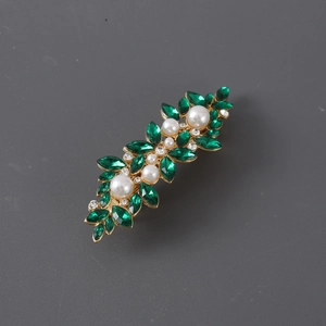 Close-up of golden hair clip with green marquise rhinestones and white pearls in leaf pattern